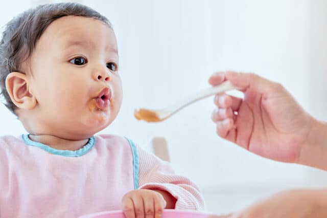 Woman holding spoon feeding baby